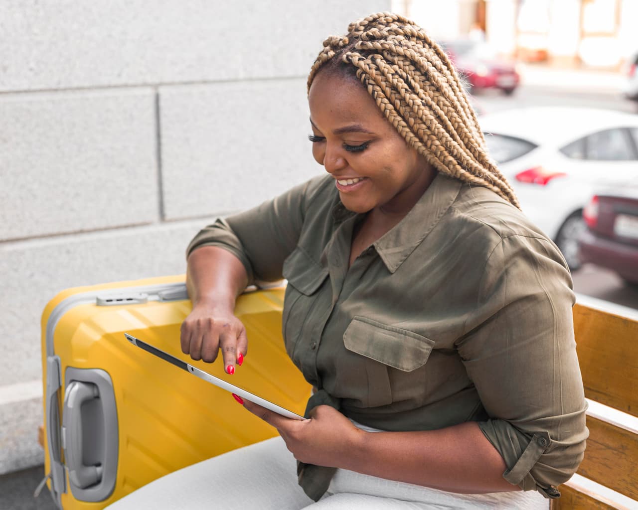 Woman with a yellow suitcase booking a trip on a tablet